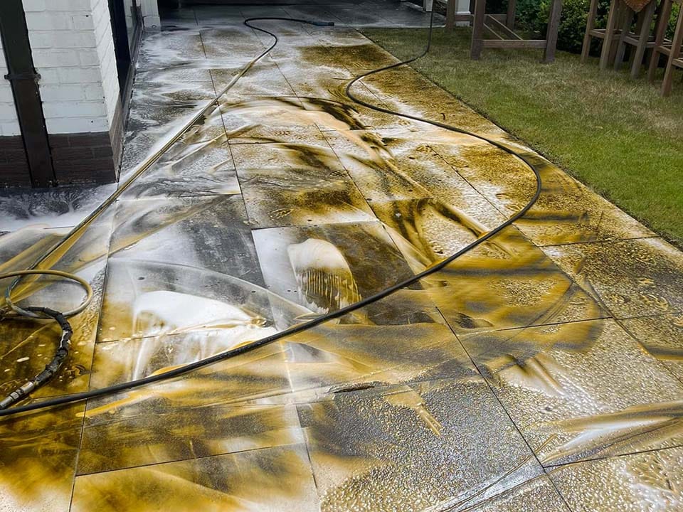 Natuurstenen terras tijdens hogedrukreiniging met schuim en losgespoeld vuil over de tegels